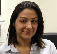 New York City: Stephanie Ueberall (headshot), director of violence prevention with Citizens Crime Commission of New York City, smiling woman with shoulder-length brown hair, necklace wearing rolled-up white shirt sitting at desk.