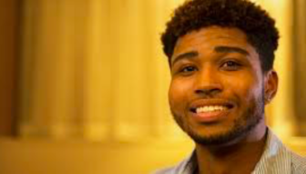 Young man looking at the camera and smiling, with short cropped hair and a small beard.