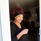 host home: Smiling woman with red hair held back by black hairband stands at door.