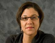 Woman looking at camera, with glasses and wearing earrings.