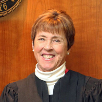 trauma-informed: Judge Ann Gail Meinster (headshot), presiding juvenile judge in the First Judicial District in Colorado, smiling woman with short red hair in white turtleneck, black judicial robes