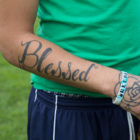 dog training: Tattoo of word blessed and flower image on right arm of someone in green shirt, blue athletic pants.