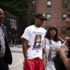 police shooting: Man in black Yankees cap has arm around older woman outside, both in T-shirts with boy’s photo on it.