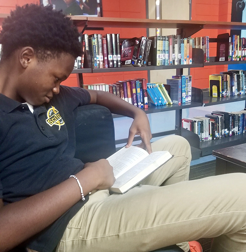 trauma: Boy in polo shirt, khaki, bracelet reads book in library