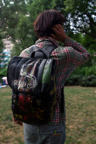 LGBTQ: Man wearing backpack stands facing away outside.