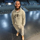 theater: Smiling young man in gray Nike sweats stands on theater stage.