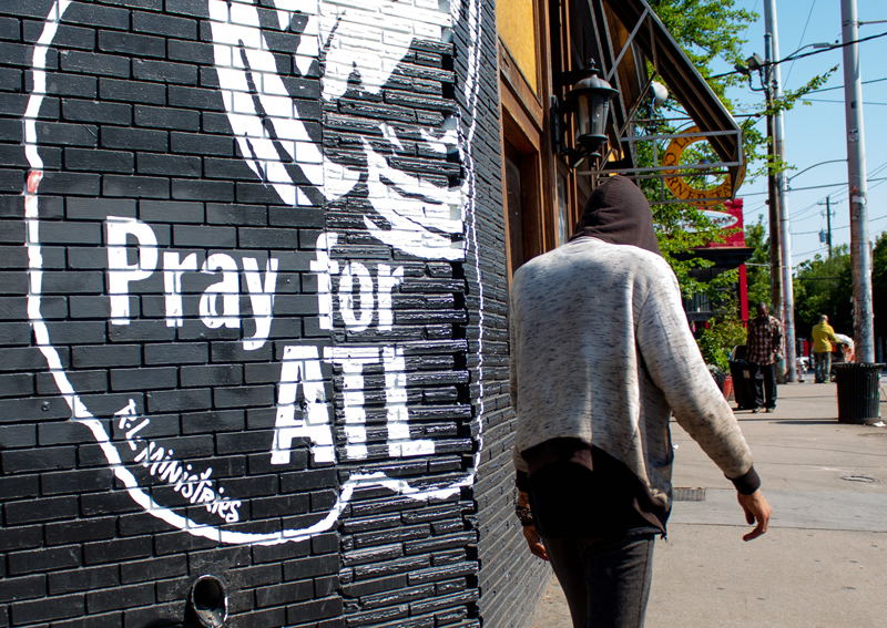 homelessness: Man in hoodie walks past mural on brick wall that says pray for atl