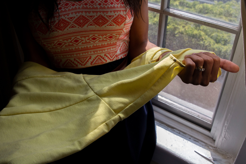 trans: Someone holds yellow dress near window.