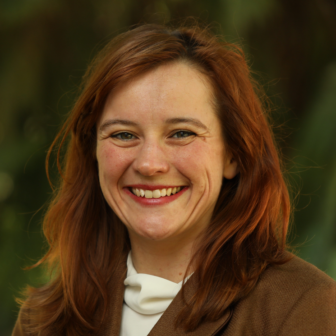parole: Kristen Bell (headshot), assistant professor at University of Oregon School of Law, smiling woman with long red hair wearing brown blazer, white top