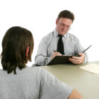 adolescent development: Man in glasses interviewing a teen and taking notes.