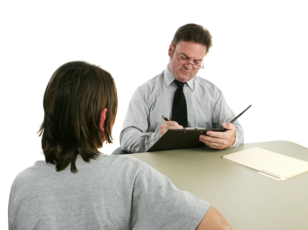 adolescent development: Man in glasses interviewing a teen and taking notes.