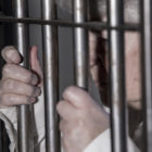 Elderly person in prison cell holding onto the bars