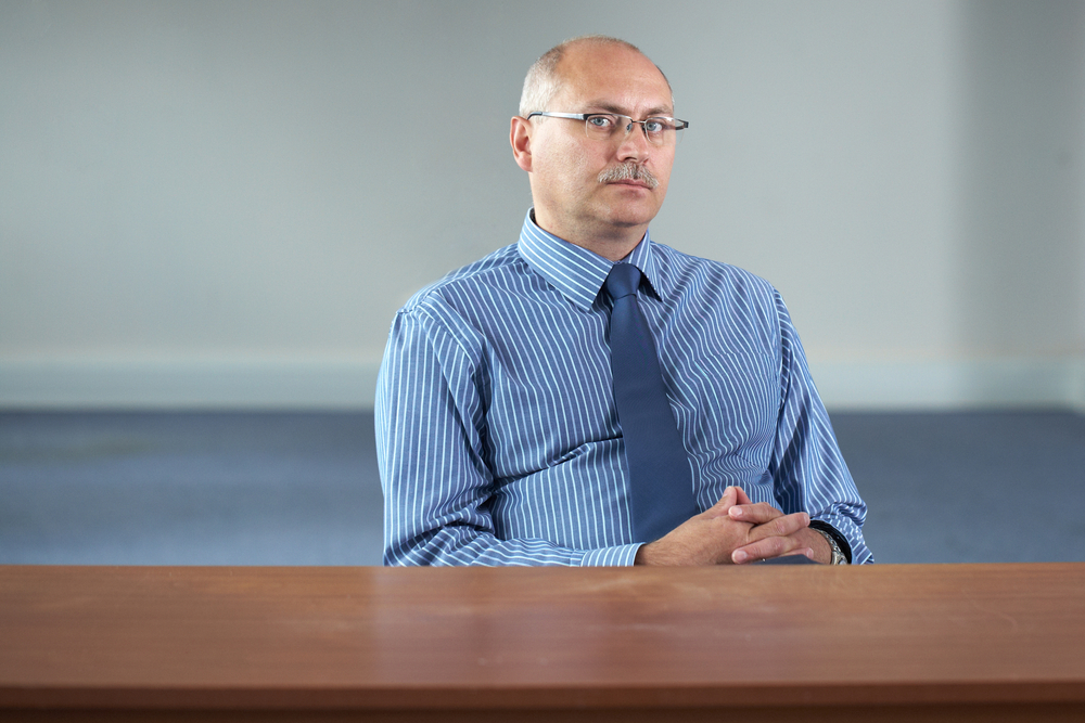 parole: Serious unsmiling balding man sits behind empty desk