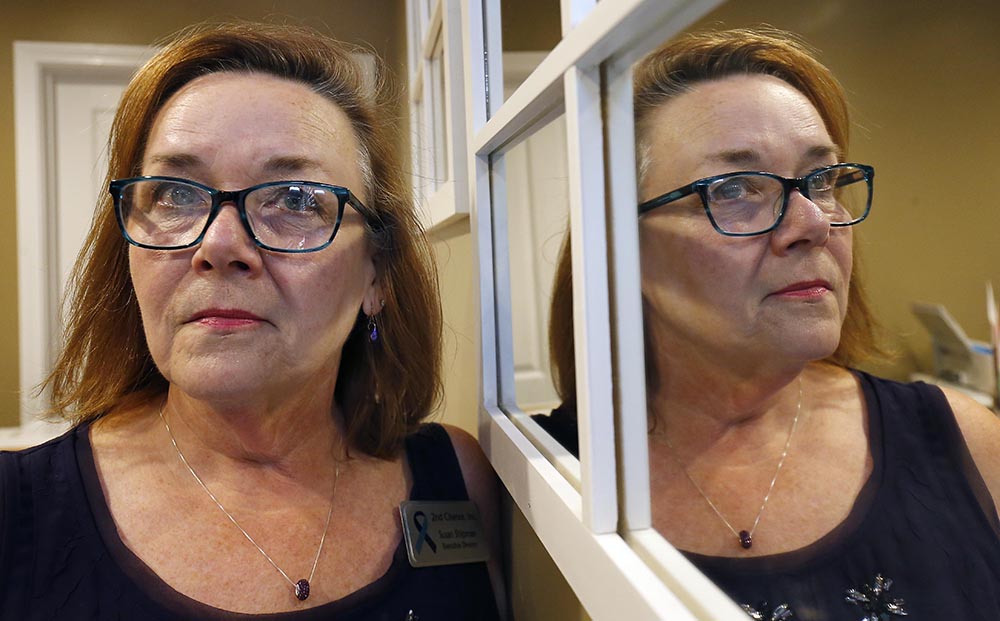domestic violence: Woman with red hair, glasses, necklace is seen both next to and reflected in mirror at right