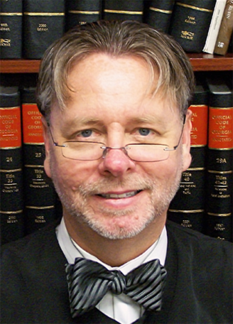 plea bargaining: Judge Steven Teske (headshot), chief judge of the Juvenile Court of Clayton County, Ga., smiling man in judge's robes, bowtie, short light brown hair, glasses halfway down nose, in front of bookcase of legal books 