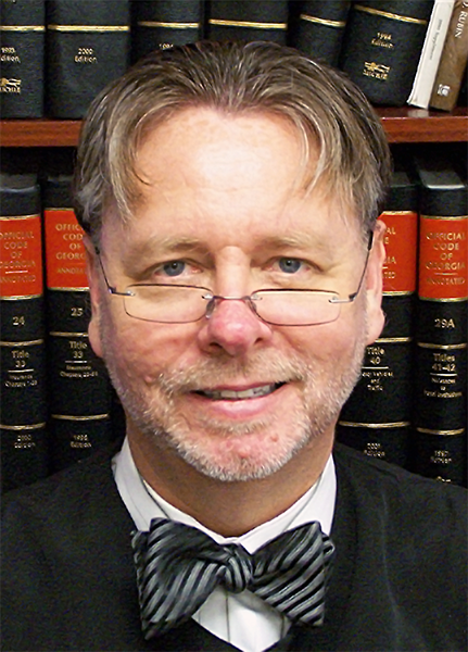 Judge Steven Teske (headshot), chief judge of the Juvenile Court of Clayton County, Ga., smiling man in judge’s robes, bowtie, short light brown hair, glasses halfway down nose, in front of bookcase of legal books