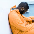 Florida: sad young african american man prisoner sitting on bench in prison cell