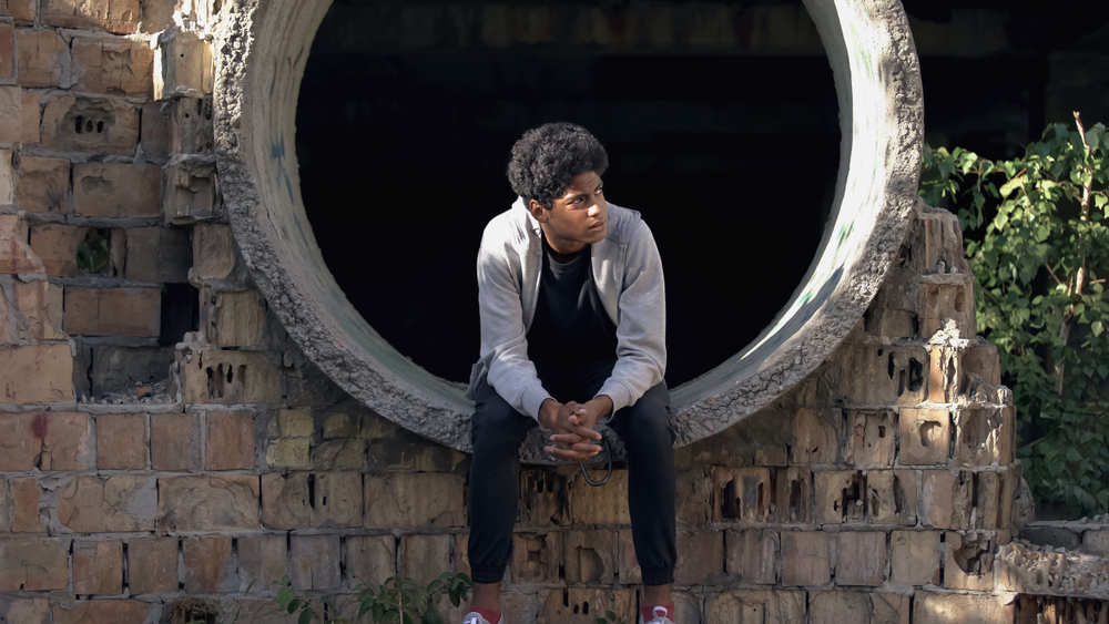 reentry: Depressed black teenager sitting in end of empty culvert