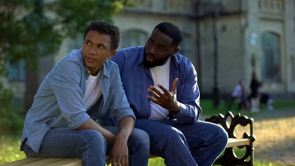transitioning: Black teenager male ignoring scolding adult sitting on bench