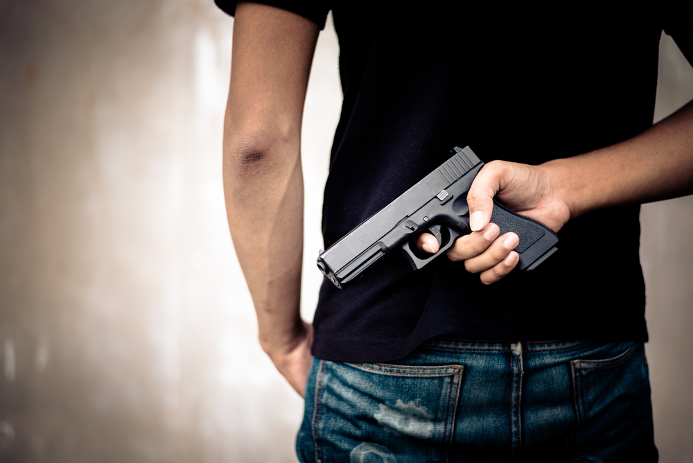 protection orders: Man in black T-shirt hiding gun behind his back.