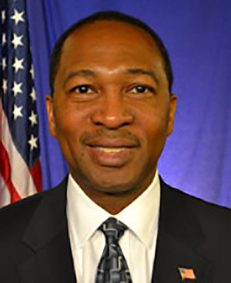 Smiling man with short hair, white shirt, dark jacket, dark patterned tie