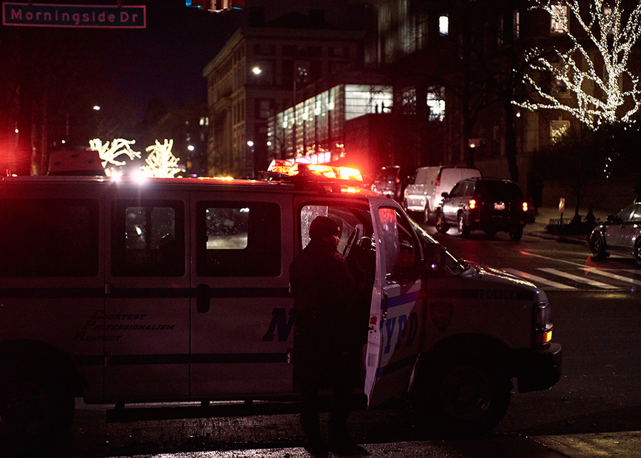 Tessa Majors: Police officer at his van on city street at night; sign says Morningside Drive