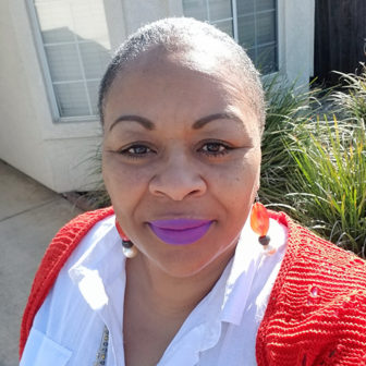 Stockton: Toni McNeil (headshot), community organizer with Faith in the Valley of San Joaquin County, woman with dark hair, necklaces, white shirt, orange sweater 
