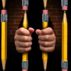 school-to-prison pipeline: photo illustration of hands clutching cell bars made of pencils with brick background