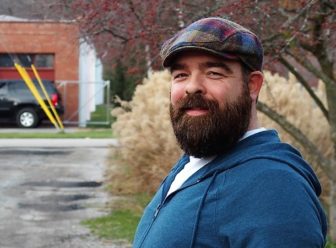 LGBTQ: Jason Melchi (headshot), owner of Empact Solutions, smiling bearded man wearing cap.