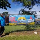 Paul Tutwiler: Man in sunglasses, blue T-shirt, black pants, brown shoes stands to left of poster on fence that says stop the gun violence Duval4life enough is enough