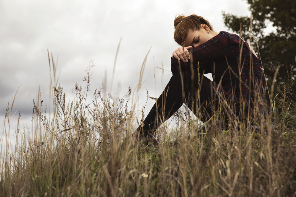 rural: Girl sits in tall grass, head down on folded arms