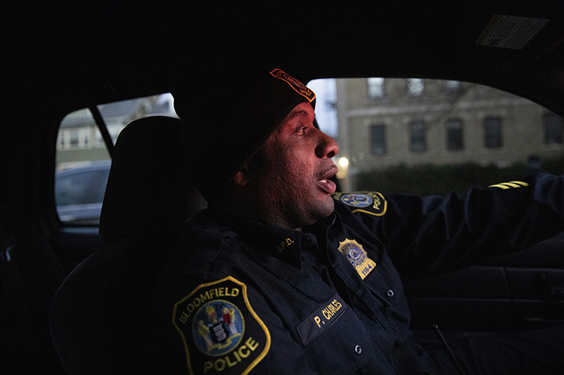Bloomfield: Police officer in cap in patrol car looks straight ahead.