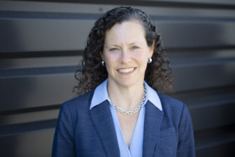 recidivism: Dana Shoenberg (headshot), senior manager at Pew Charitable Trusts’ public safety performance project, smiling woman with long dark curly hair, necklace, earrings, wearing dark blue jacket, light blue shirt