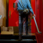 homeless: Person in jean jacket climbing stairs; tray of filled brown bags on landing