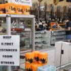 gun violence: Gun store with 2 people at counter standing next to each other and sign saying keep 6 foot distances from others.