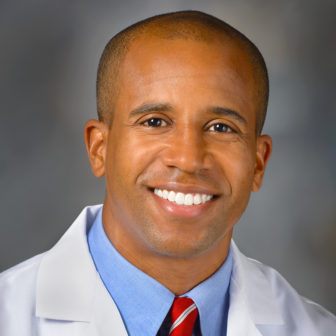 doctor: Dr. Edjah Ndudom (headshot), man smiling wearing blue top and white coat