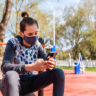 doctors: A teenager with a ponytail on his head, wearing a medical mask, sits and uses a mobile phone. Horizontal bars in the background.