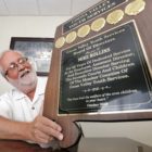Alabama: Man with white beard, mustache, wearing glasses, white shirt holds up plaque.