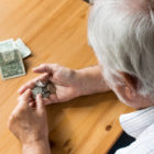 fees and fines: Man with gray hair counts dollars and coins at table