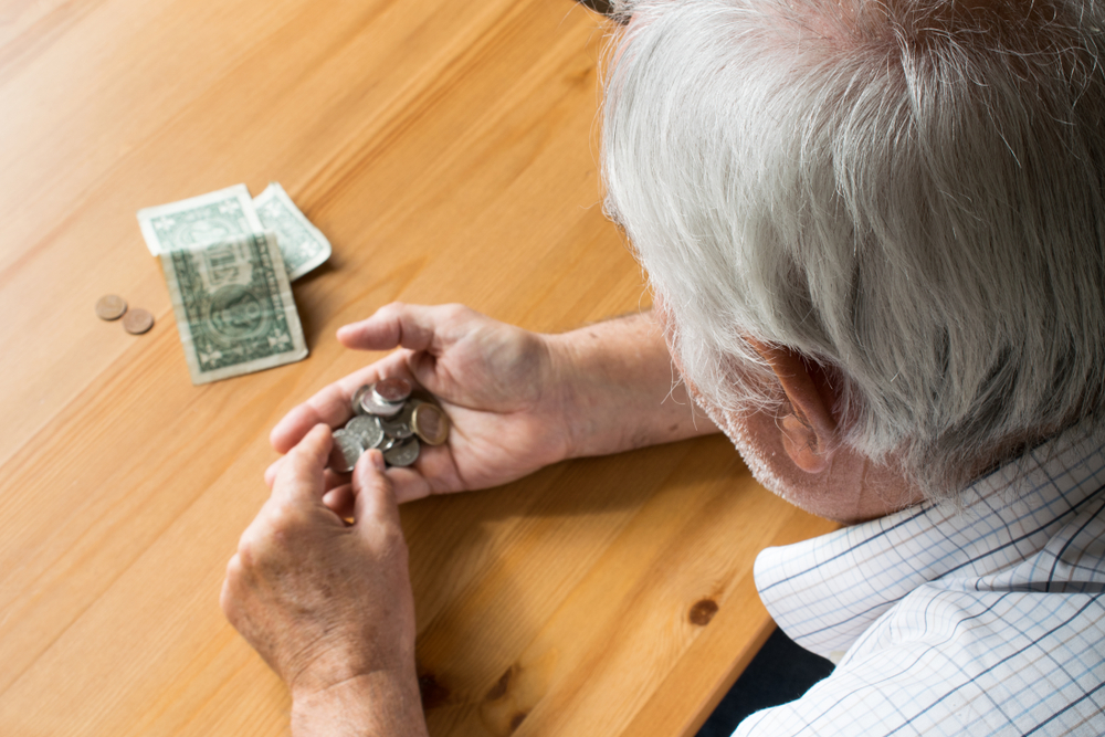 fees and fines: Man with gray hair counts dollars and coins at table