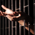 COVID-19: pleading hands of prisoner sticking through bars.