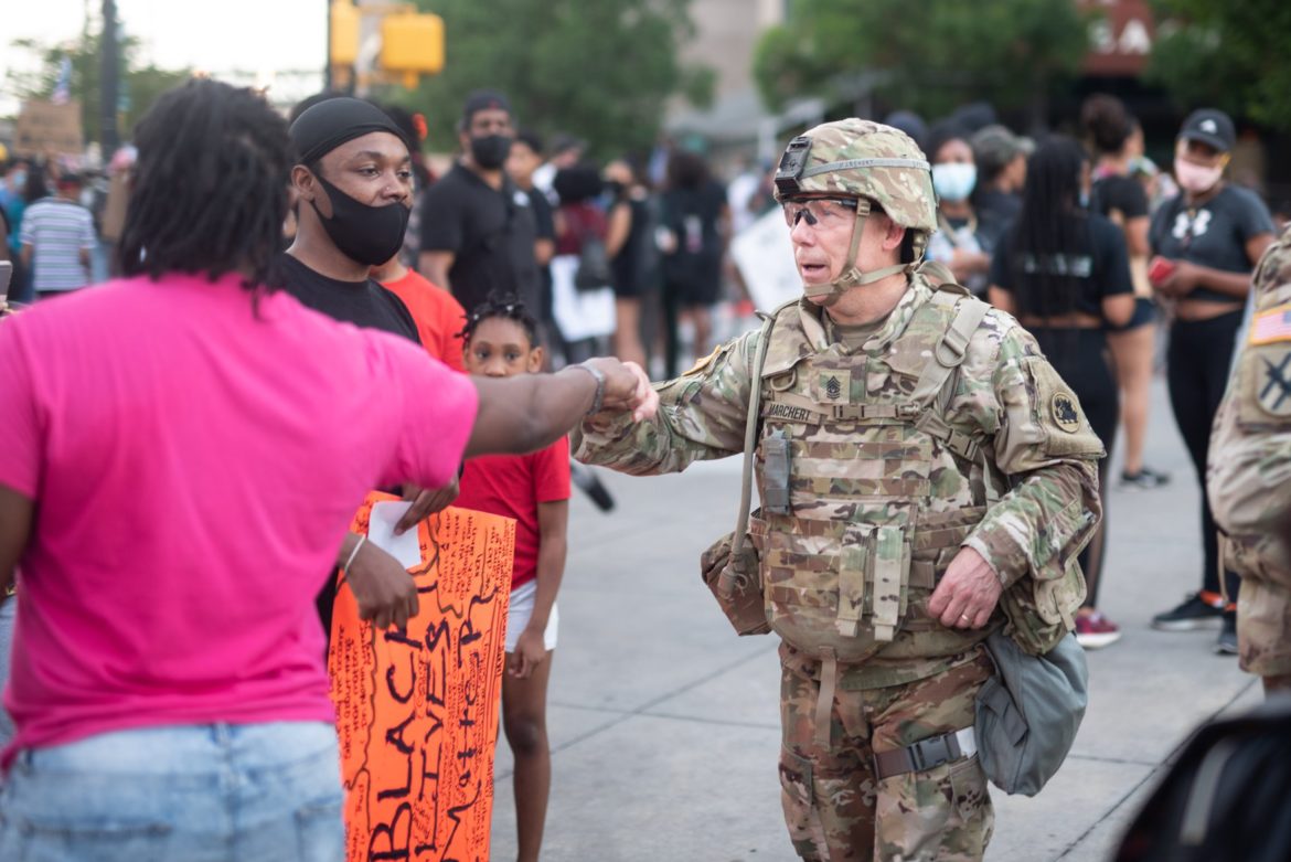 probation: Man in pink T-shirt, jeans bumps fist with member of National Guard at protest.
