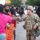 probation: Man in pink T-shirt, jeans bumps fist with member of National Guard at protest.