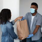 gun violence: Food delivery during coronavirus. Black courier guy wearing medical mask delivering grocery order to young woman's home