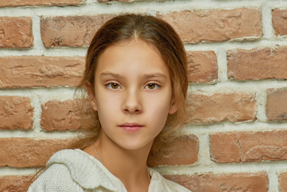 specialty court: little girl with calm look near brick wall.