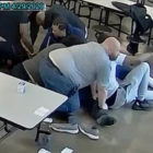 restraints: Several male adults hold down someone in jeans.