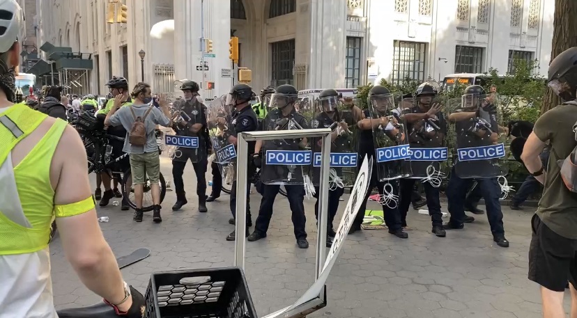 tag: Line of police hold up riot shields on city street.