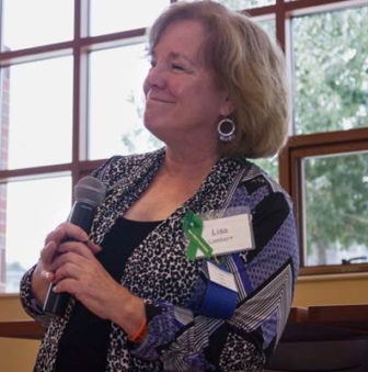 alt text: PPAL: Lisa Lambert (headshot), executive director of Parent/Professional Advocacy League, smiling woman holding mic with light brown bob, earrings, wearing multicolored jacket over black top