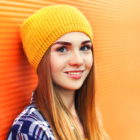 Young blonde woman wearing yellow hat against orange wall background