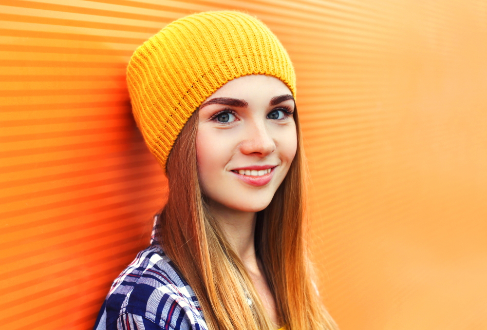 Diversion: Young blonde woman wearing yellow hat against orange wall background
